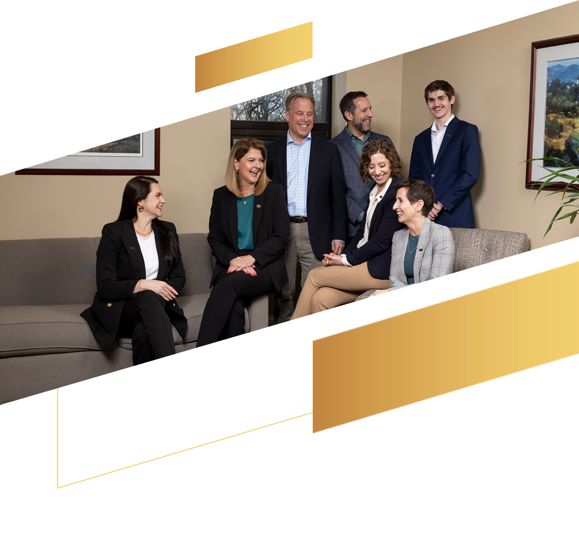 Six professionally dressed people smile and talk together in a modern office with framed art on the walls, discussing financial planning and services.