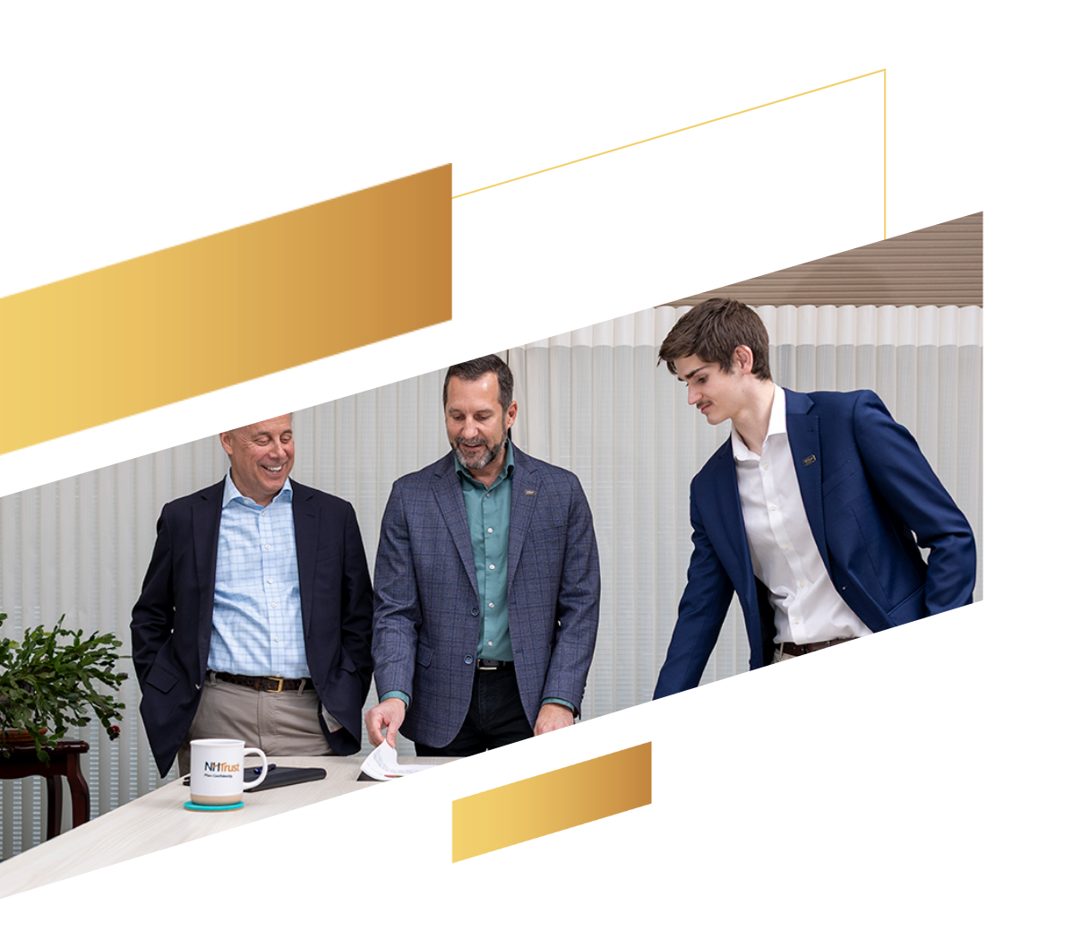 Three men in business attire stand and smile around a table in a modern office with gold geometric accents.