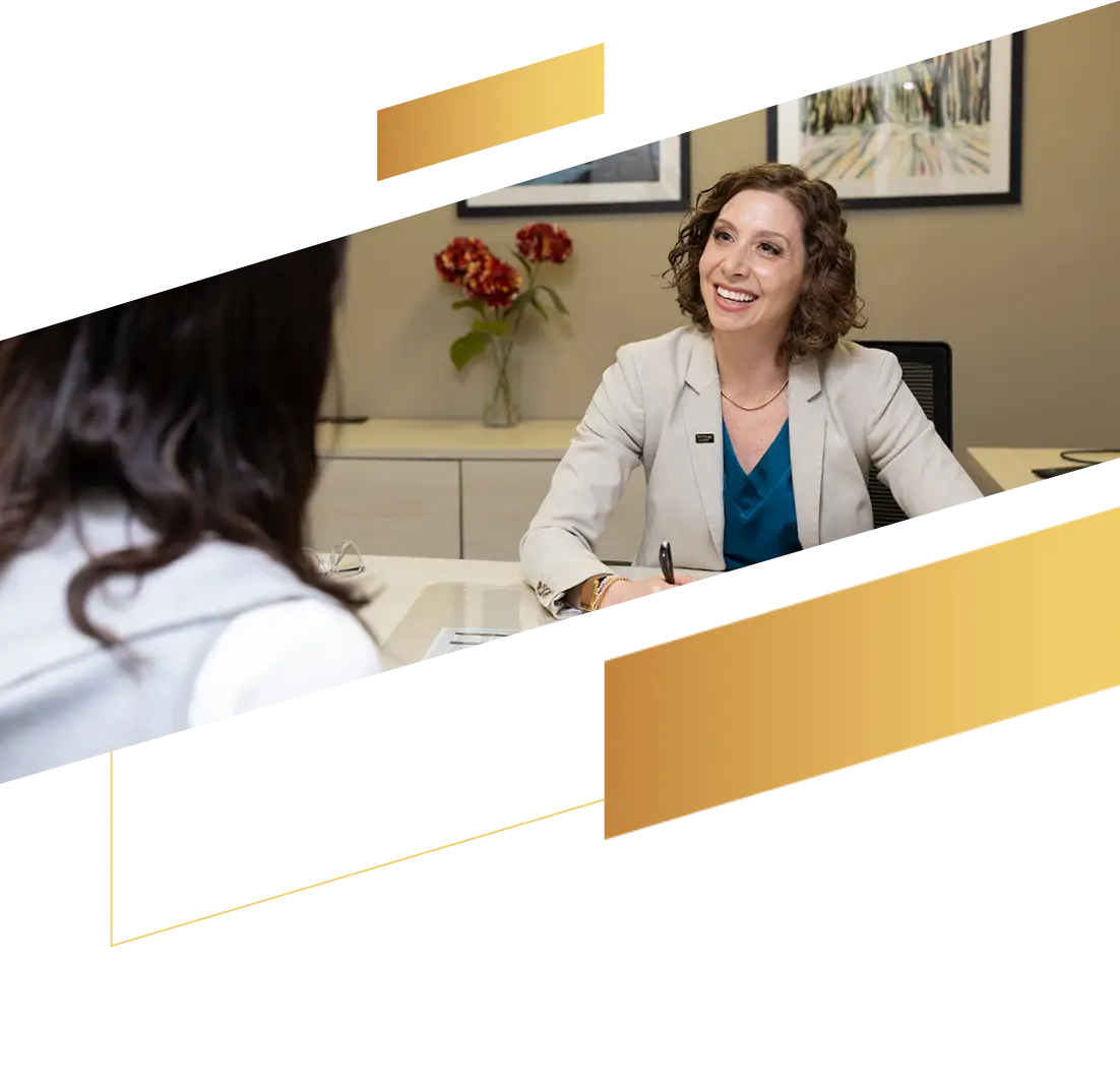 A woman in a suit smiles while talking to another person across a desk in a modern office.