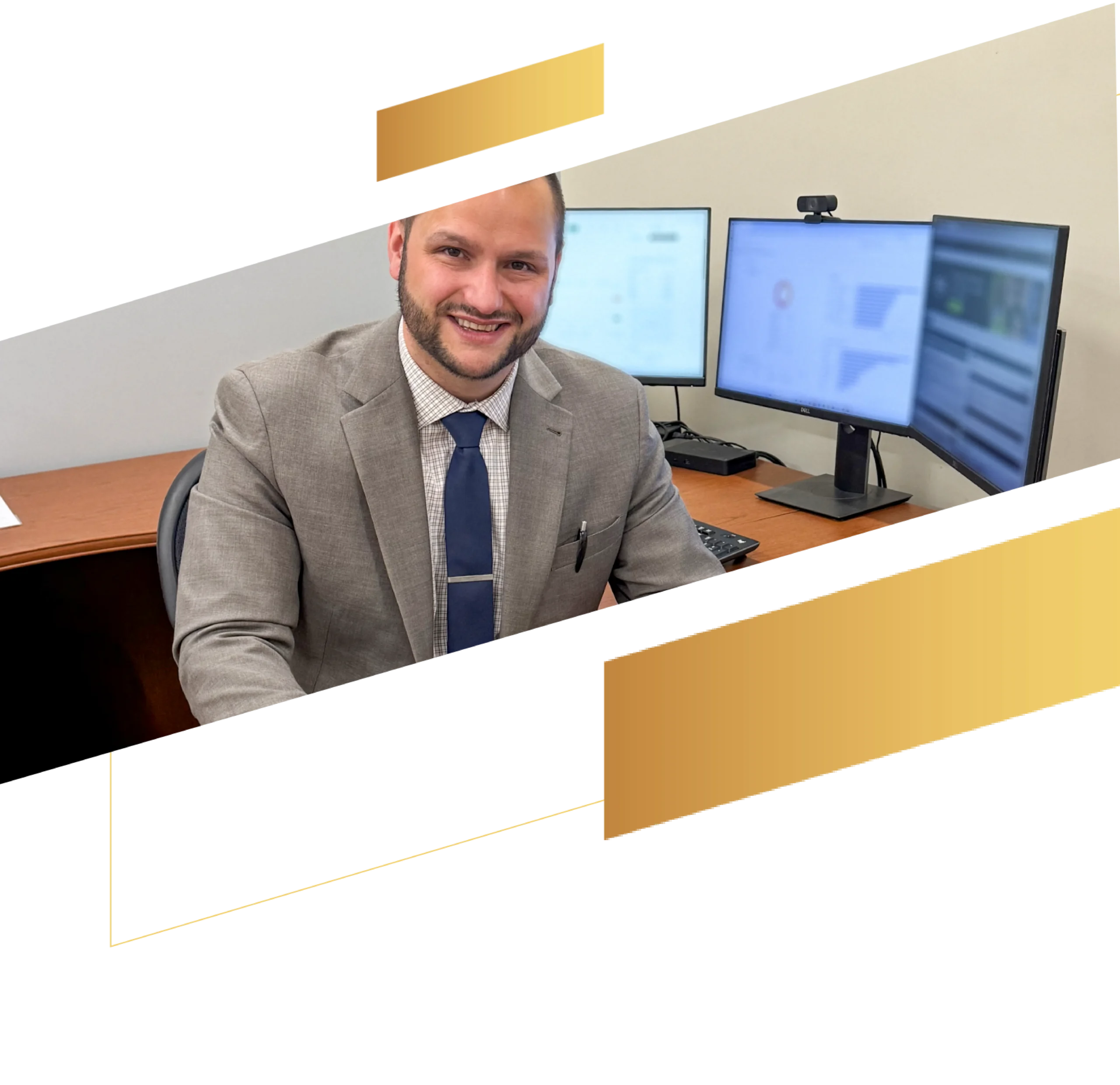 A man in a suit smiles at a desk with two computer monitors, suggesting a modern insurance office, with gold geometric shapes overlaying the image.