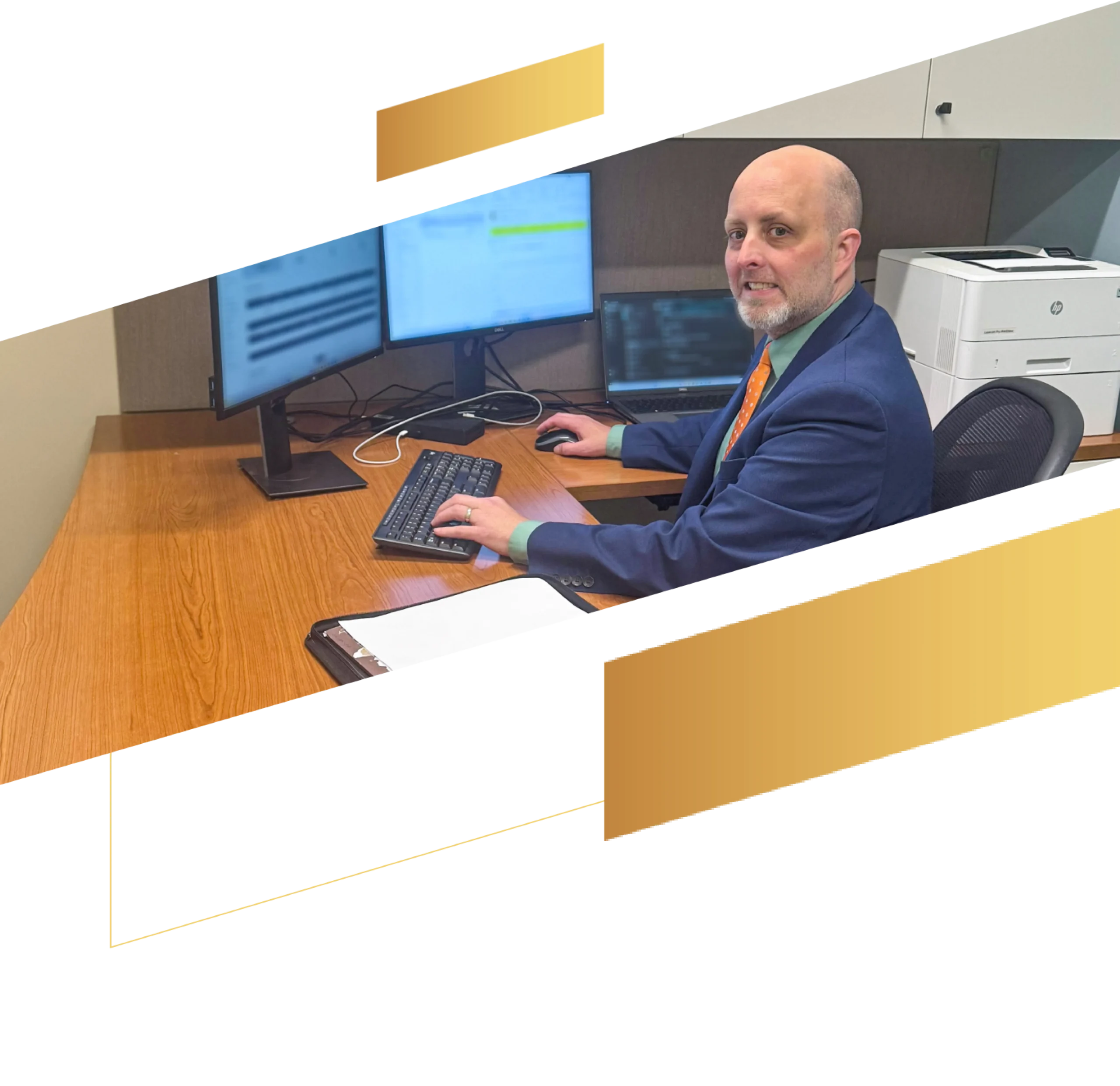 A man in a suit works at a desk with three monitors and a printer, smiling at the camera as he reviews documents for UGMA and UTMA accounts.