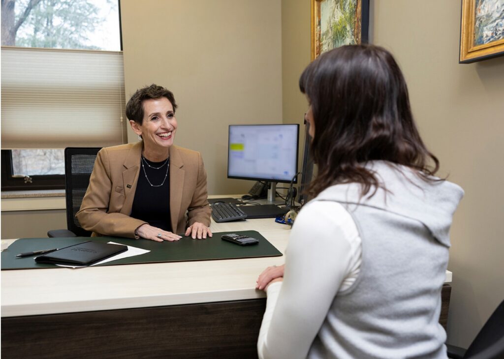 Two people sit across a desk in an office, having a friendly conversation.