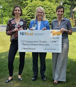 Three women outdoors hold a large $25,000 check made out to Cheshire Health Foundation from NH Trust.