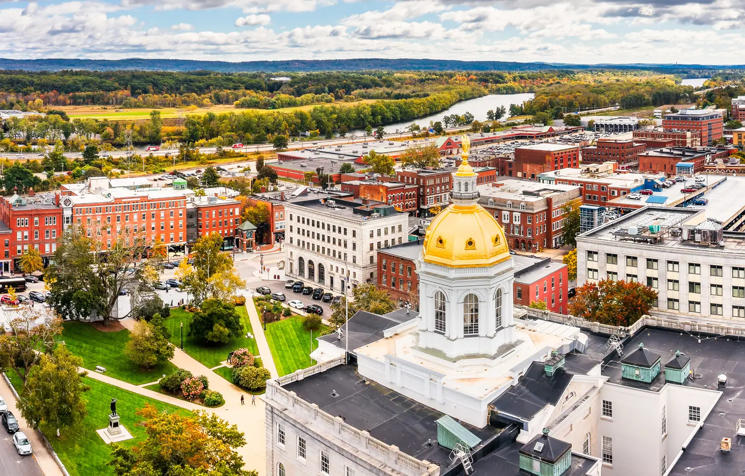 Aerial view of a city with a gold-domed capitol building, red brick buildings, and green trees in autumn.